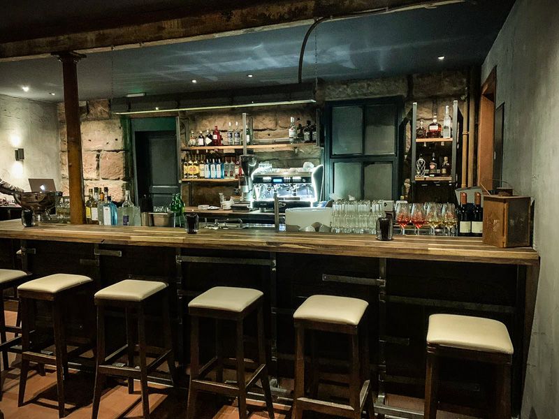 Theke mit Barhockern, dahinter Regale mit Flaschen und eine Kaffeemaschine