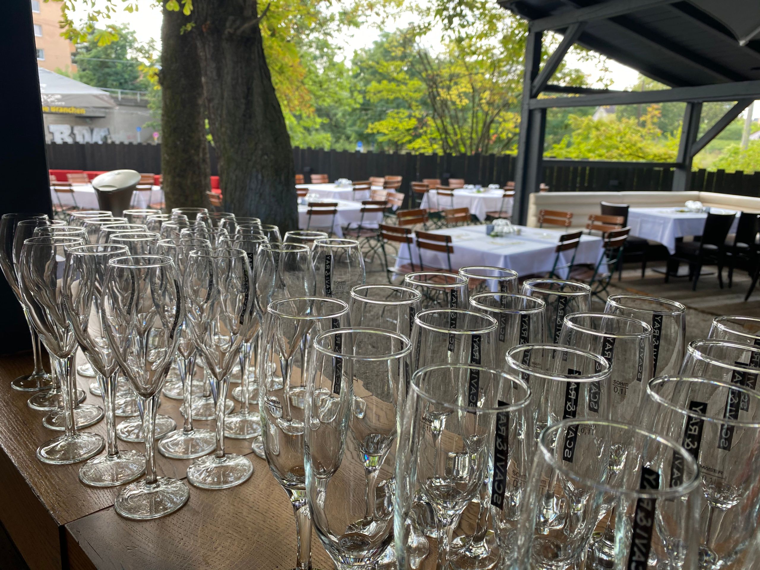 Reihen von Sektgläsern, im Hintergrund der Biergarten mit gedeckten Tischen