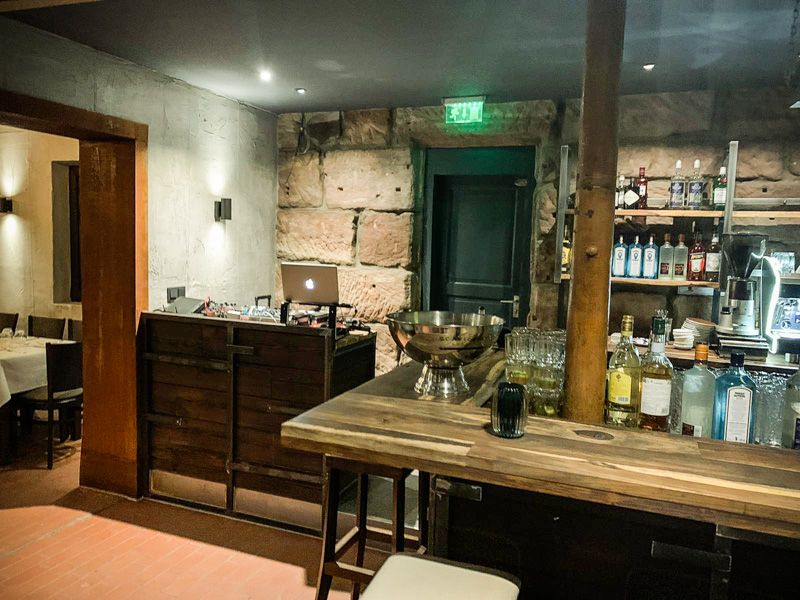 Bartheke aus Holz mit Flaschen, dahinter ein DJ-Pult mit Laptop vor der Natursteinwand